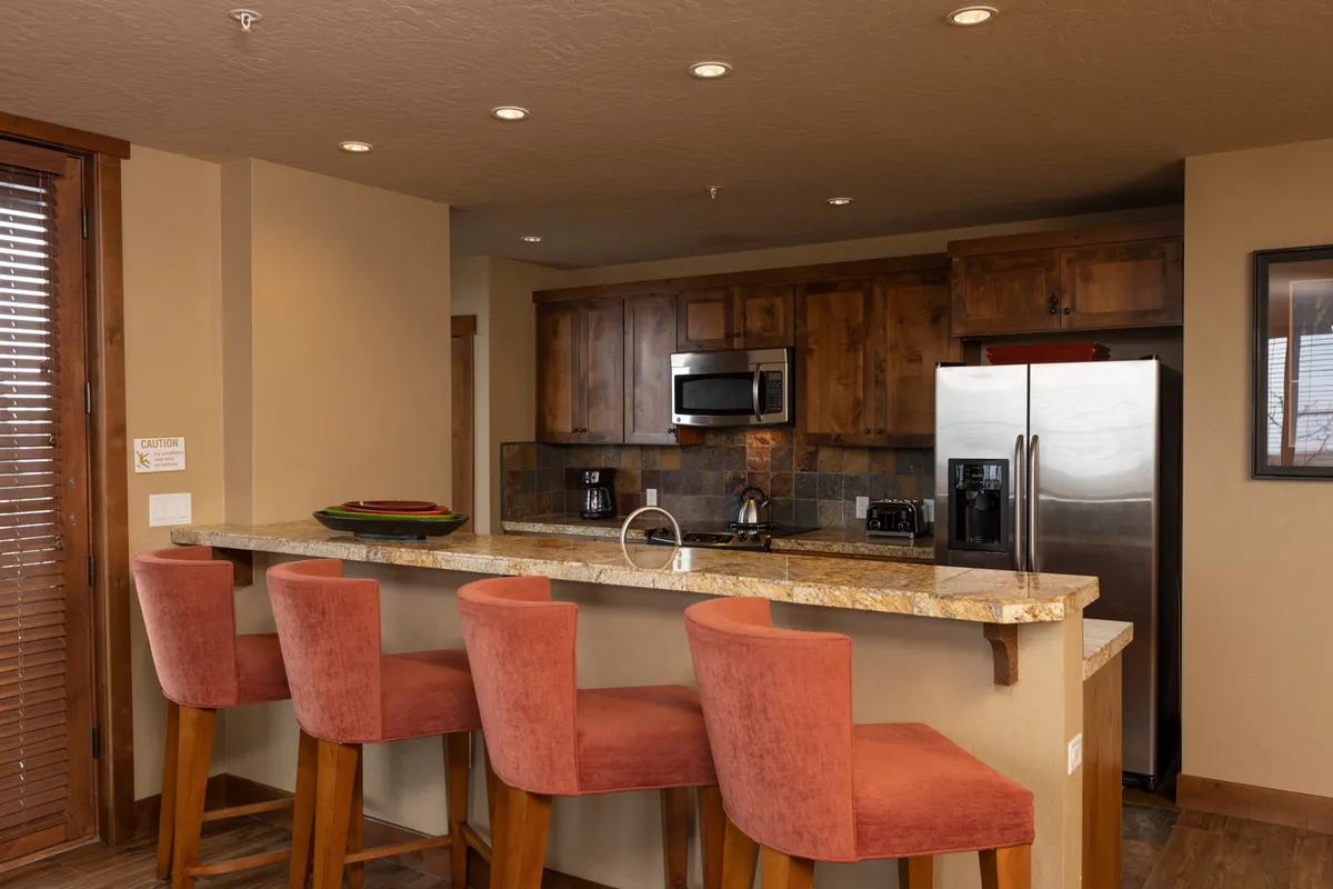 An inviting interior social space featuring a stylish bar counter with stool seating, kitchen appliances, and warm lighting. The scene suggests a cozy spot for morning coffee, evening cocktails, and shared meals, ideal for couples or small groups to unwind together.