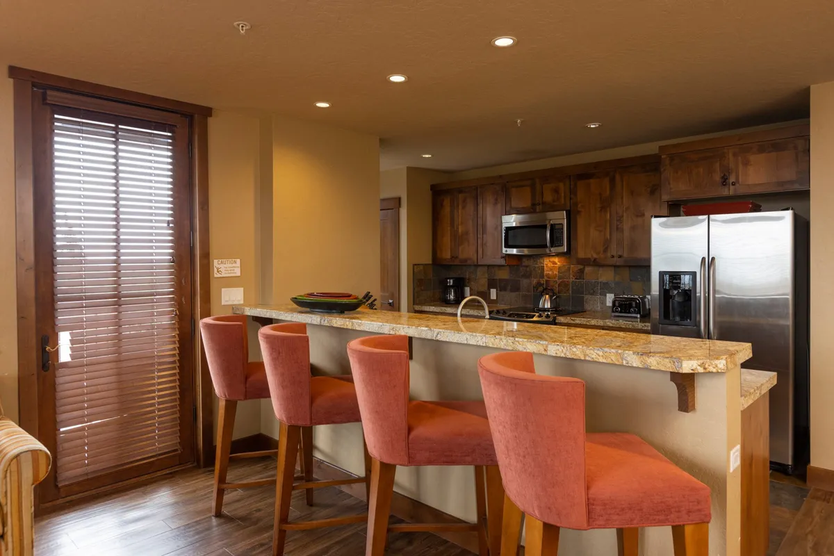 A modern kitchen space with a bar counter and stools, granite countertops, and stainless steel appliances. The layout encourages conversation and social interaction, with a seamless connection to the living and dining areas.