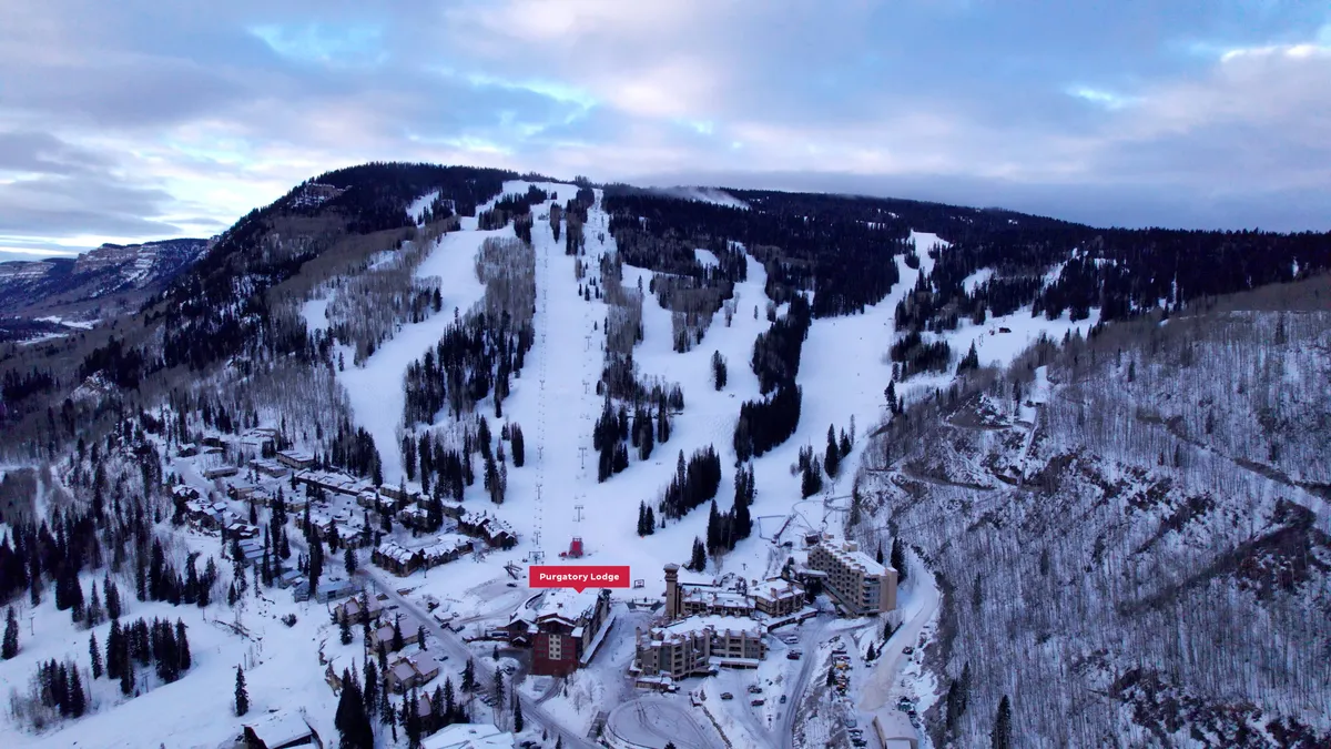 A sweeping exterior shot of Purgatory Lodge nestled among the snow-covered slopes, with the majestic San Juan mountains as a dramatic backdrop. The image showcases skiers on the slopes, the inviting lodge, and the surrounding winter wonderland, perfectly capturing the thrill of ski-in, ski-out access and the cozy retreat waiting at the base.