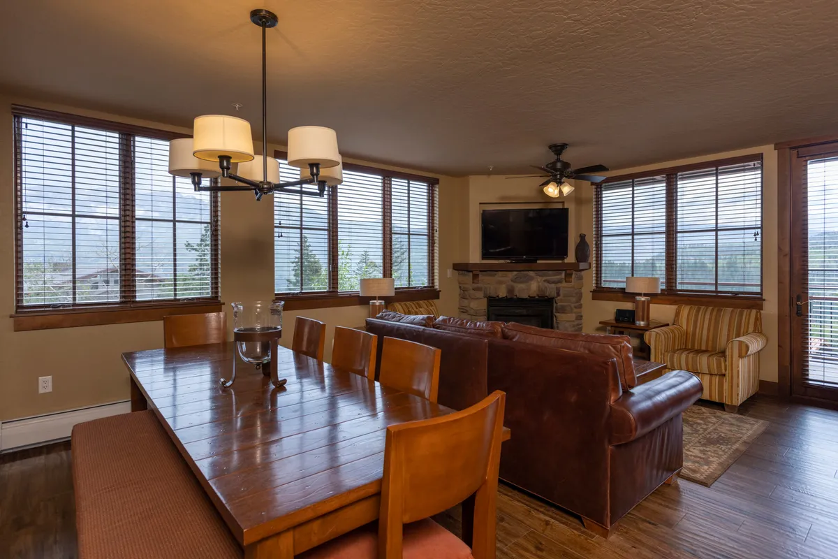 A spacious living space seamlessly combines a dining area and comfortable seating arranged around a gas fireplace. Large windows flood the room with natural light and provide vistas of the surrounding mountains, while the elegant dining table is set for memorable meals and social gatherings.