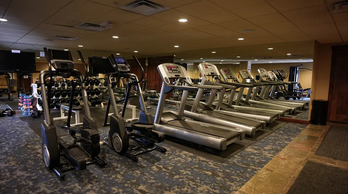 This interior shot features a modern fitness center with treadmills, elliptical machines, and a dumbbell rack. The environment is bright and motivational, catering to guests who want to maintain their workout routines while on vacation.