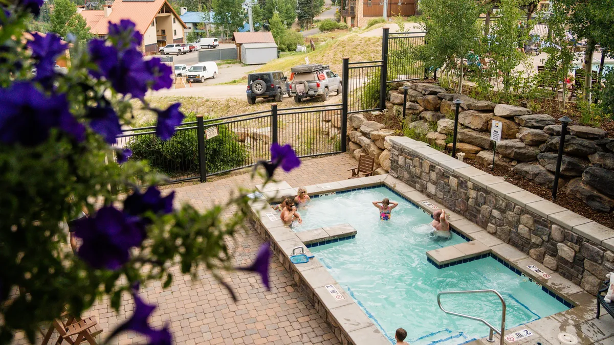 This image showcases a lively outdoor swimming pool surrounded by colorful flowers, with several people enjoying the water and lounging by the poolside. The pool area feels cheerful and inviting, embodying the resort's focus on family fun and relaxation.